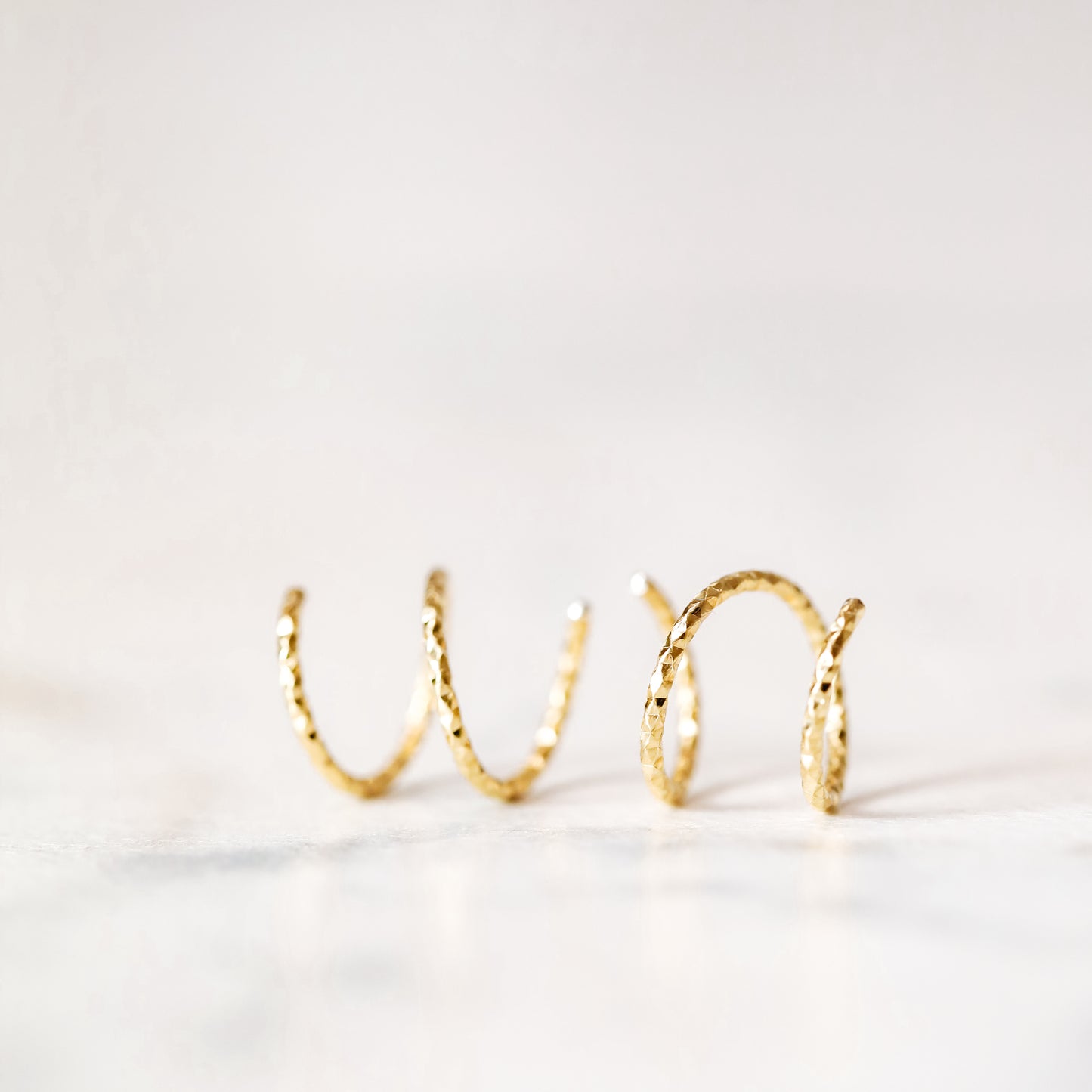 Minimal gold double hoop earrings with spiral twist design worn on ear, illusion of double piercing, diamond cut sterling silver jewelry