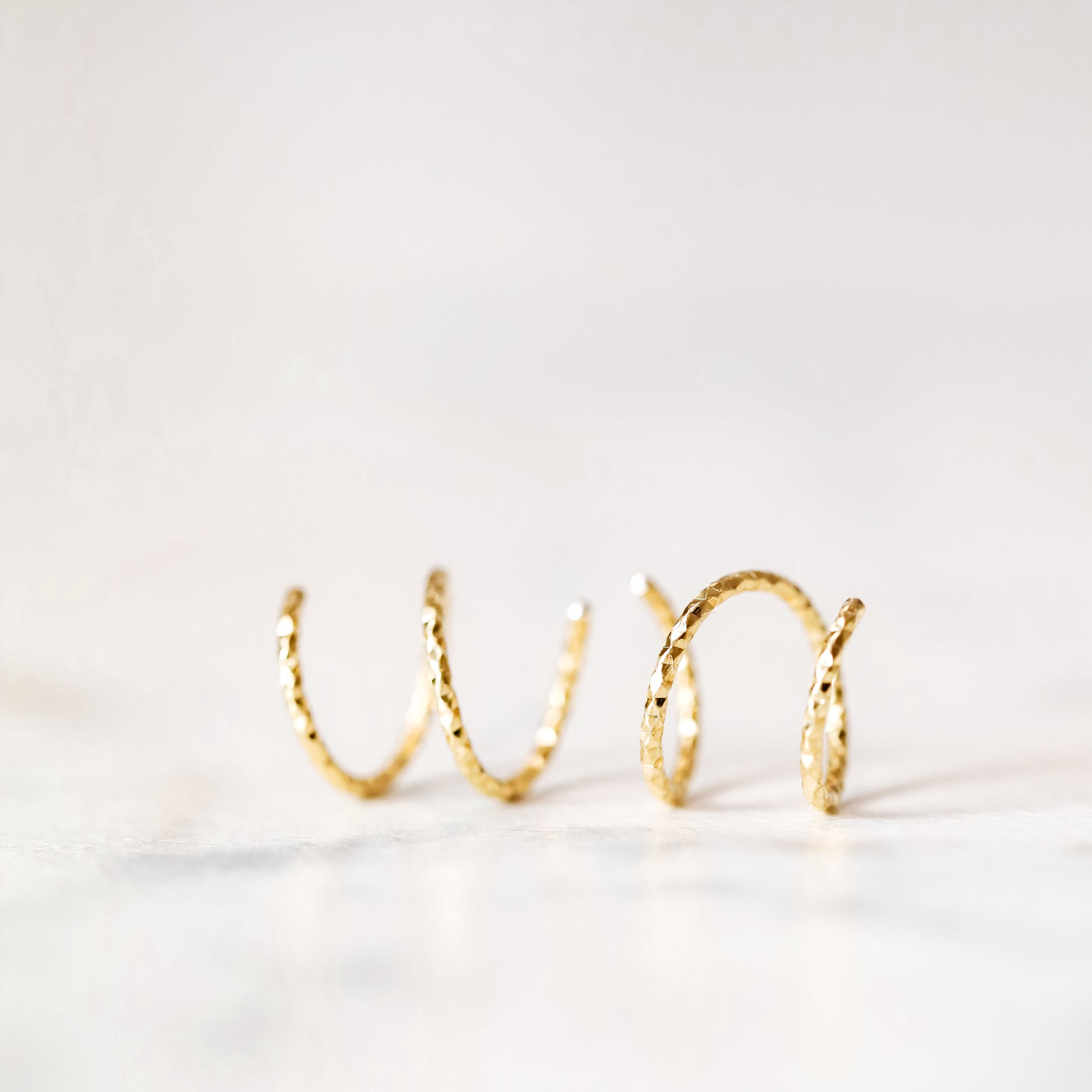 Minimal gold double hoop earrings with spiral twist design worn on ear, illusion of double piercing, diamond cut sterling silver jewelry