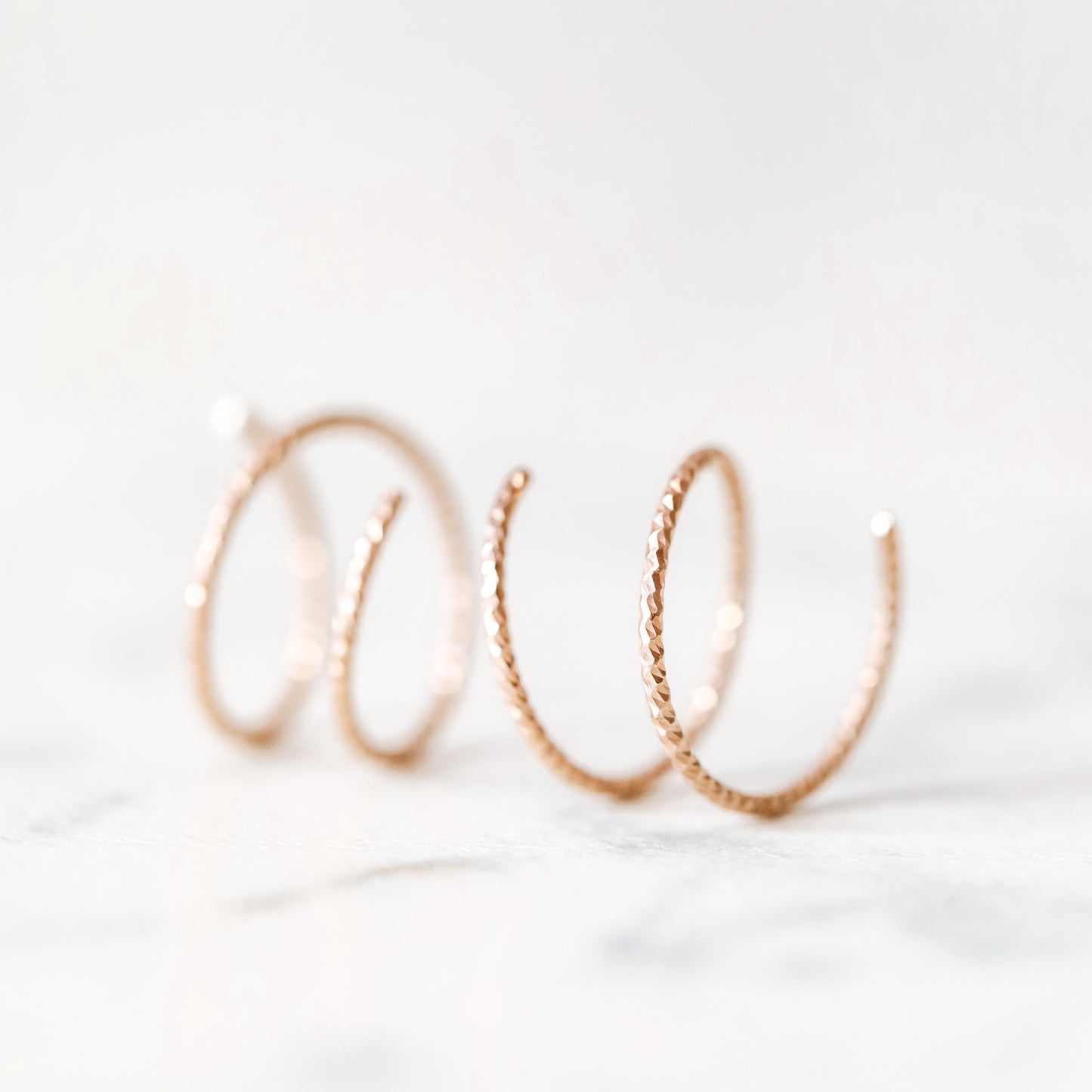Close-up of a woman's ear wearing tiny rose gold double hoop illusion earrings with a diamond-cut texture, designed to create the appearance of two piercings with a single hole.