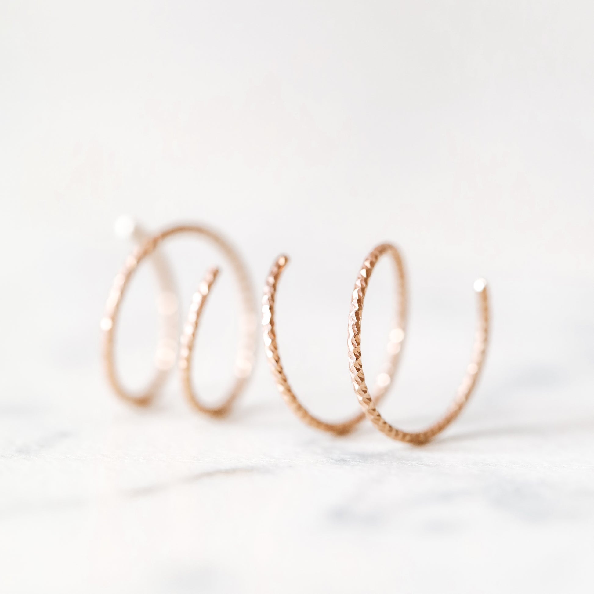 Close-up of a woman's ear wearing tiny rose gold double hoop illusion earrings with a diamond-cut texture, designed to create the appearance of two piercings with a single hole.