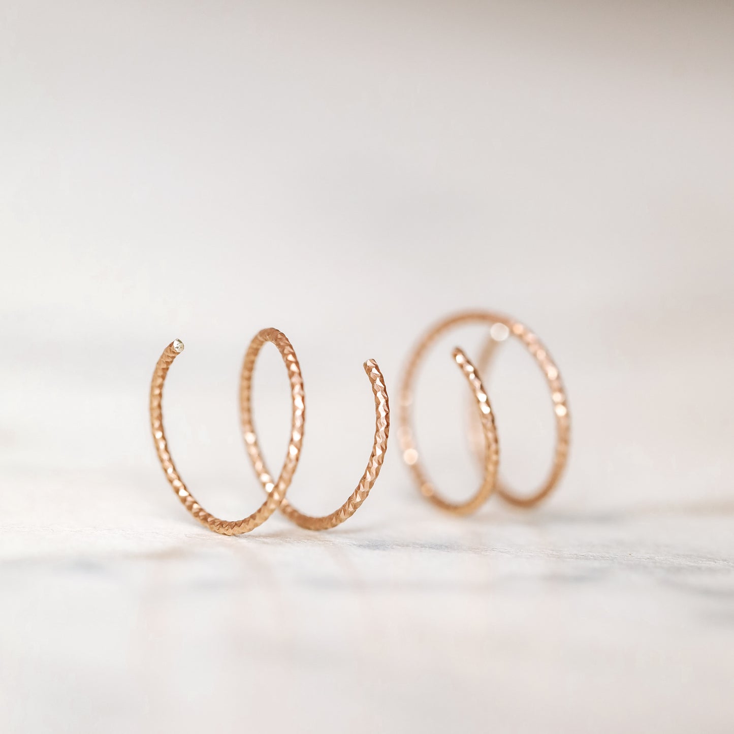 Close-up of a woman's ear wearing tiny rose gold double hoop illusion earrings with a diamond-cut texture, designed to create the appearance of two piercings with a single hole.