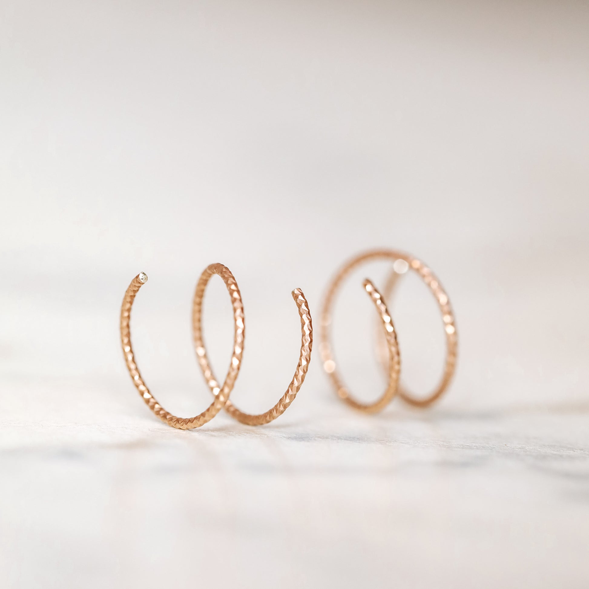 Close-up of a woman's ear wearing tiny rose gold double hoop illusion earrings with a diamond-cut texture, designed to create the appearance of two piercings with a single hole.