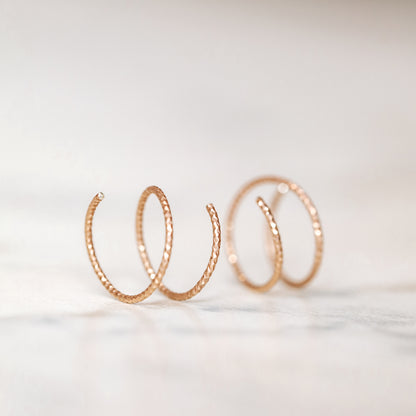 Close-up of a woman's ear wearing tiny rose gold double hoop illusion earrings with a diamond-cut texture, designed to create the appearance of two piercings with a single hole.