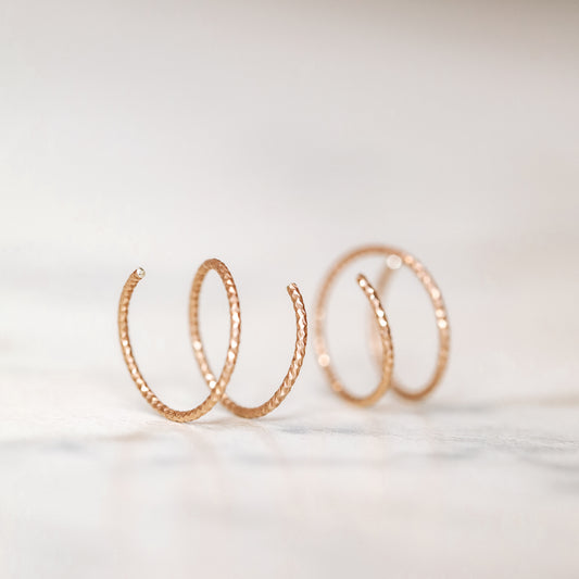 Close-up of a woman's ear wearing tiny rose gold double hoop illusion earrings with a diamond-cut texture, designed to create the appearance of two piercings with a single hole.