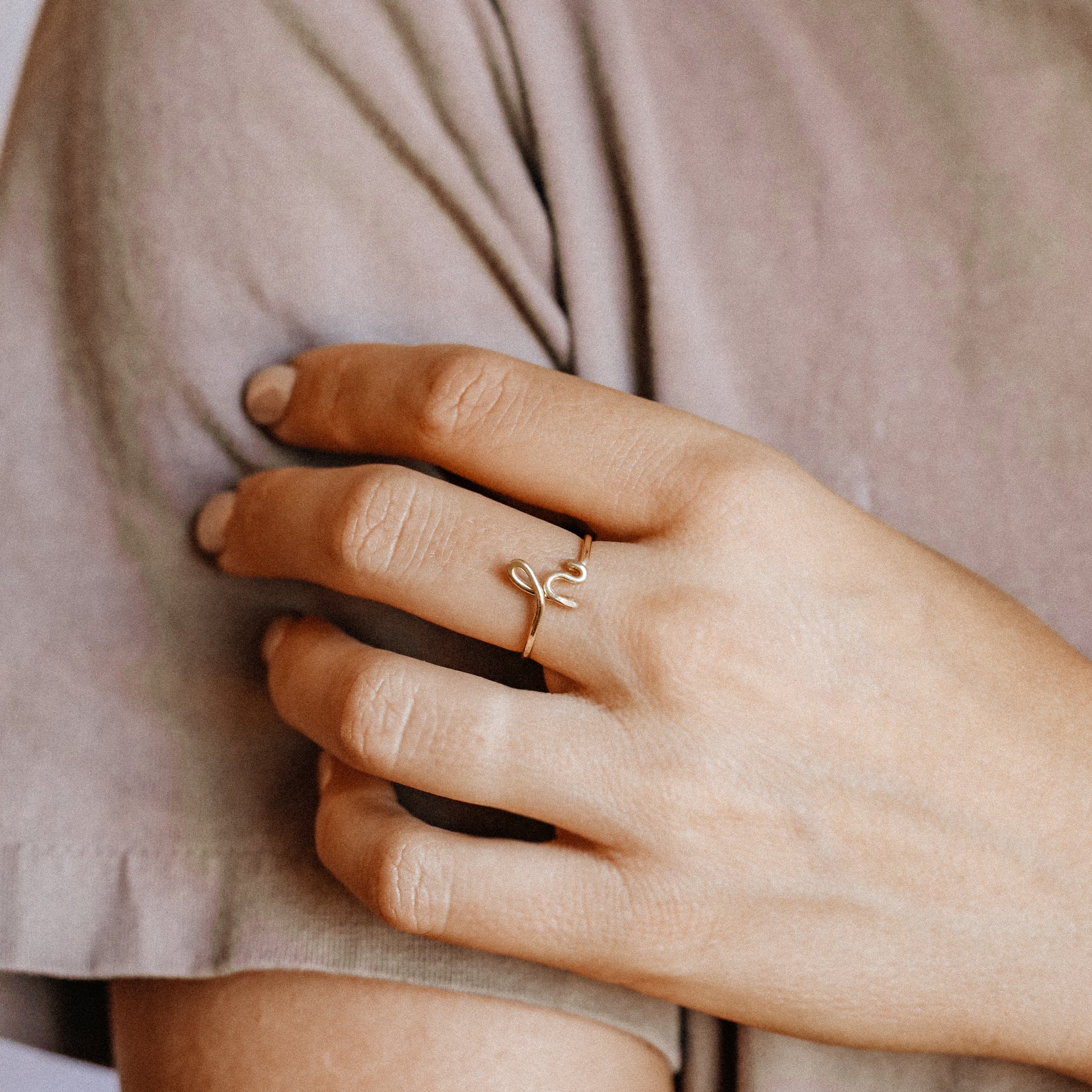 Close-up of a handmade 14k gold filled wire ring shaped into the letter H on a woman's finger.