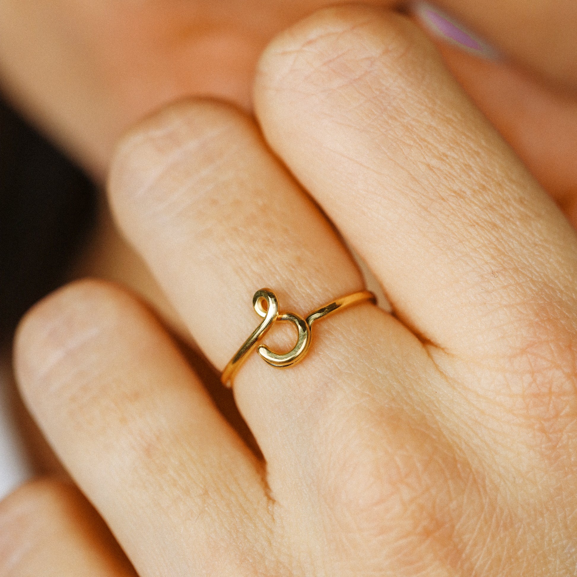 Handheld view of a delicate handmade cursive lowercase letter S adjustable ring in gold, featuring a minimalist wire design.