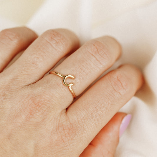 Delicate handmade gold wire ring with a lowercase cursive letter C, worn on a hand.