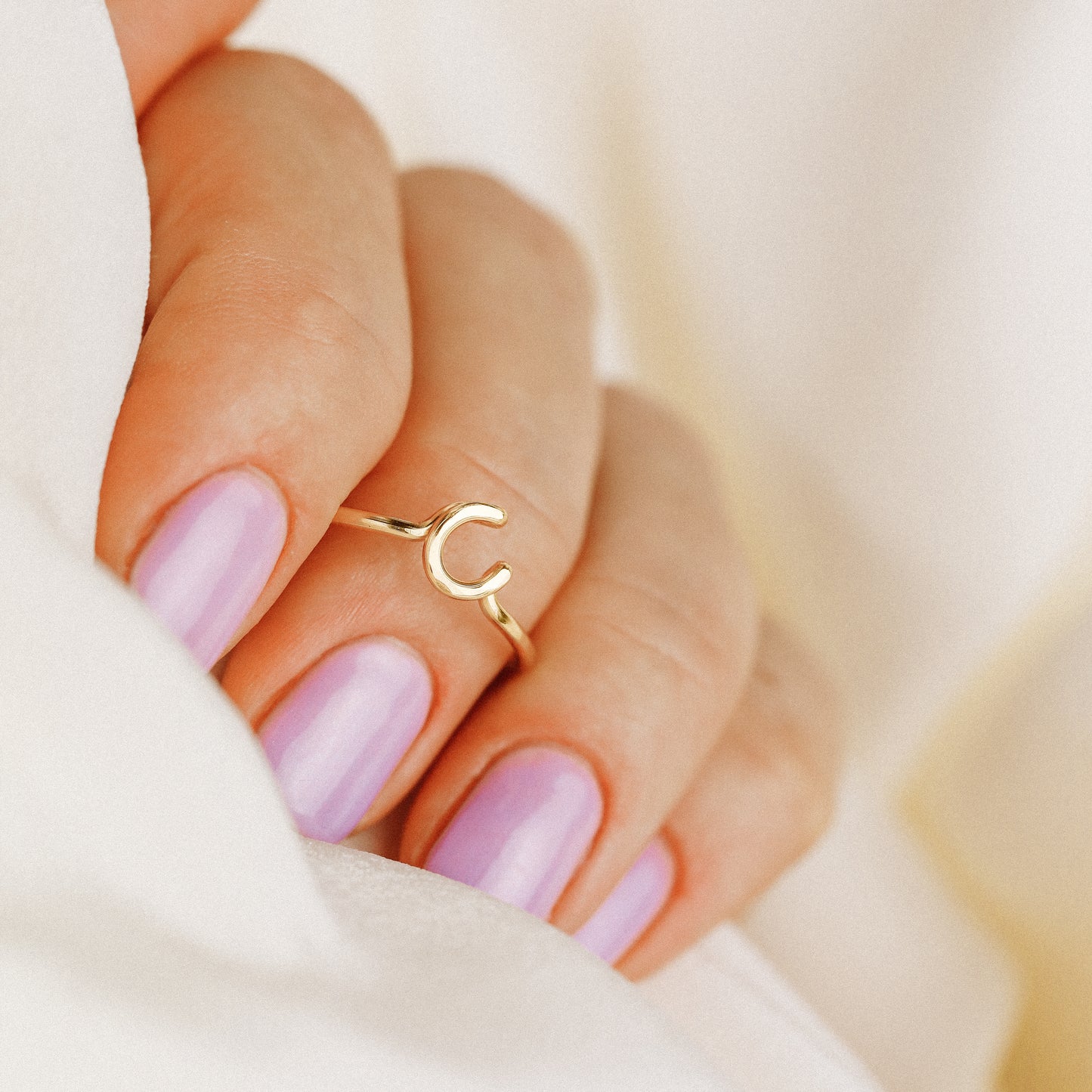 Close-up of a handmade 14k gold filled wire ring shaped into the letter C on a woman's finger.