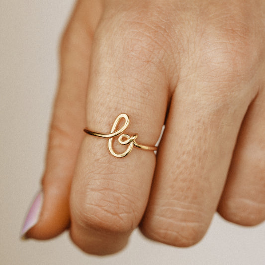 Close-up of a handmade 14k gold filled wire ring shaped into the letter B on a woman's finger.