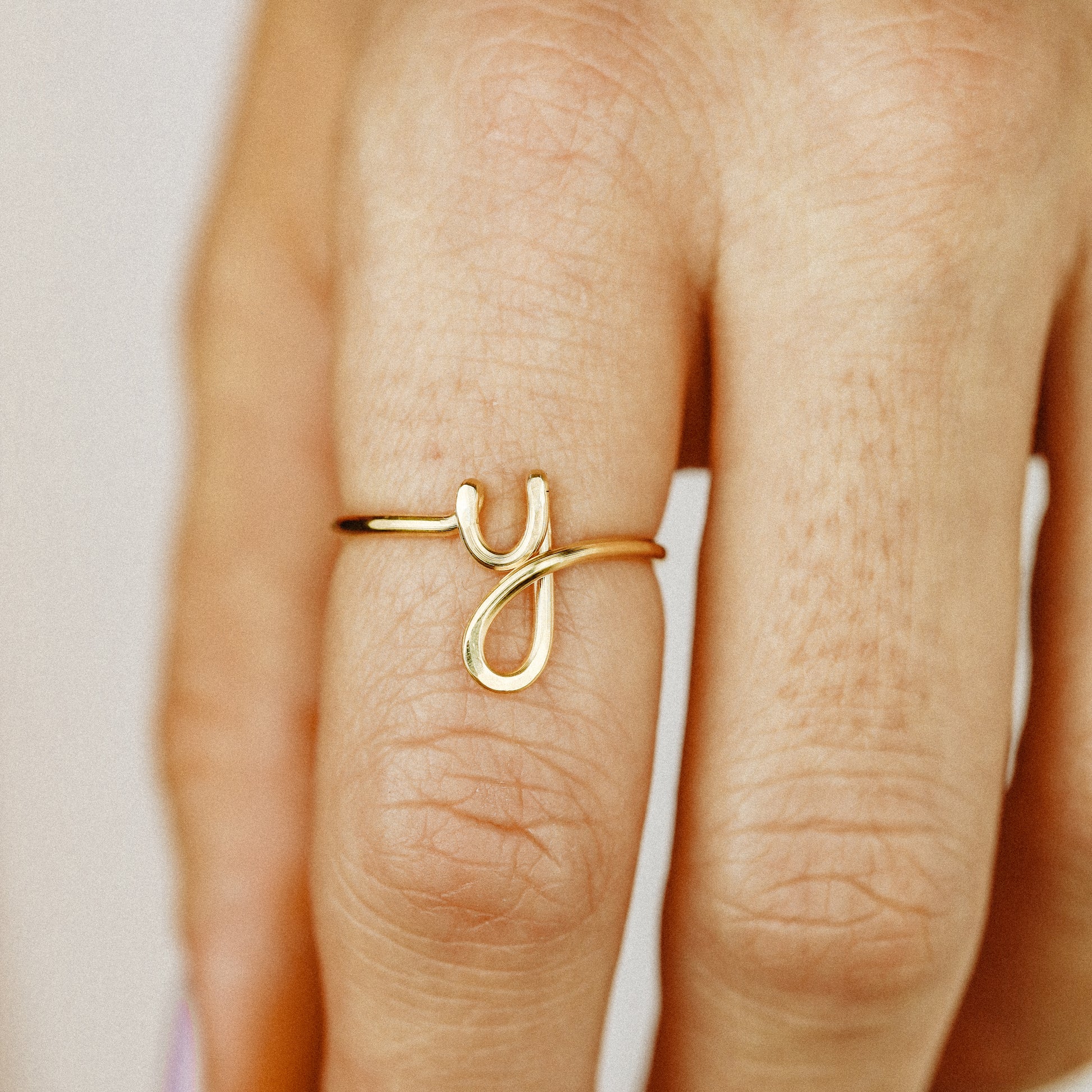 Close-up of a handmade 14k gold filled wire ring shaped into the letter Y on a woman's finger.