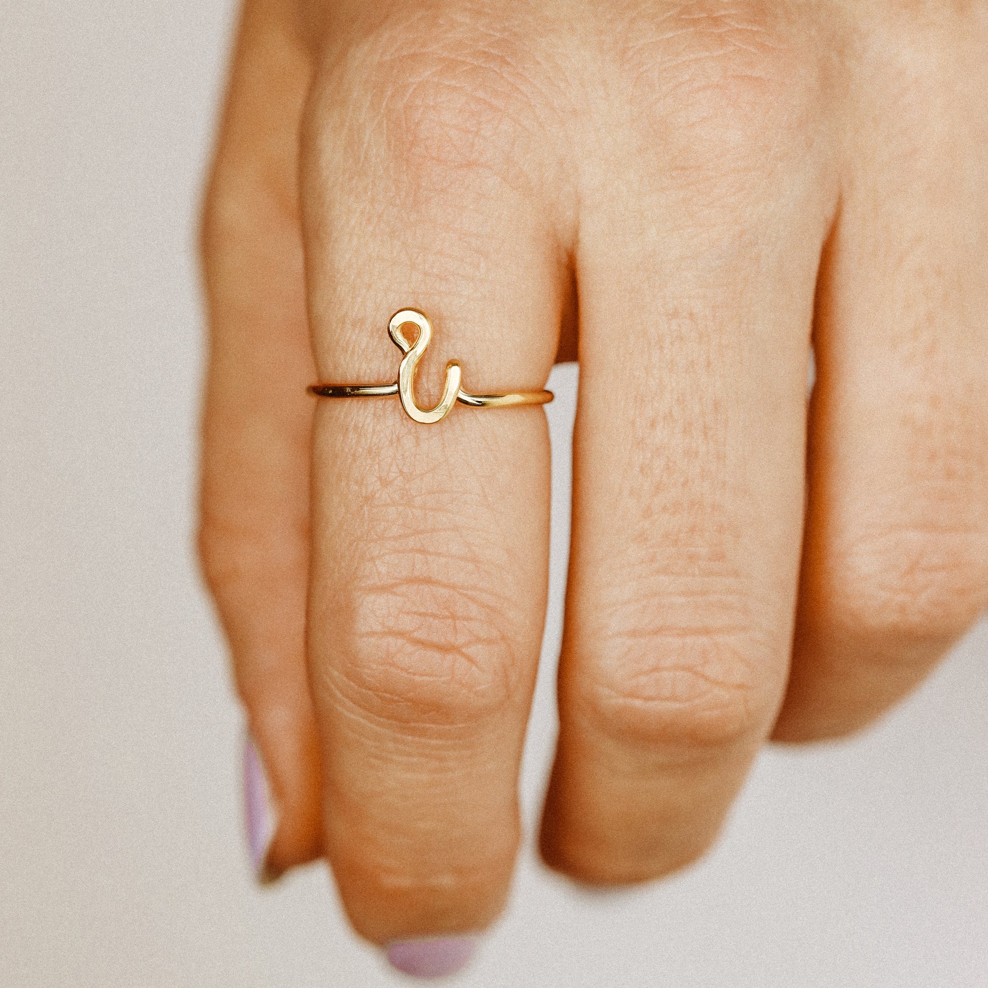 Handmade dainty gold wire ring with a lowercase cursive letter i, worn on a hand with elegant nails.