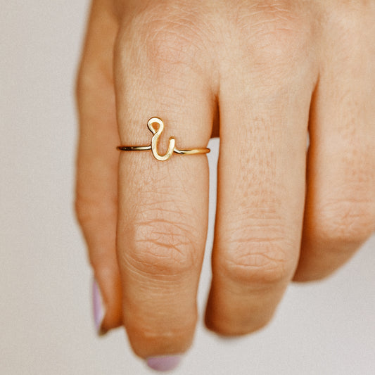 Handmade dainty gold wire ring with a lowercase cursive letter i, worn on a hand with elegant nails.