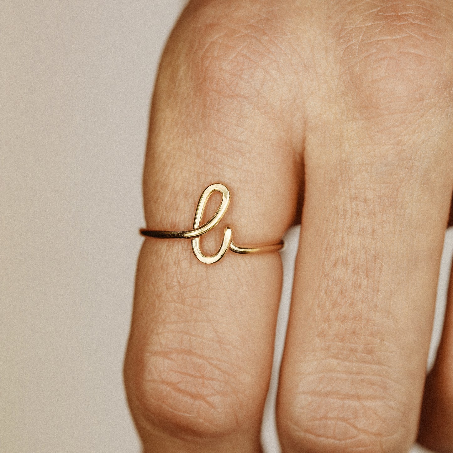 Close-up of a handmade 14k gold filled wire ring shaped into the letter L on a woman's finger.