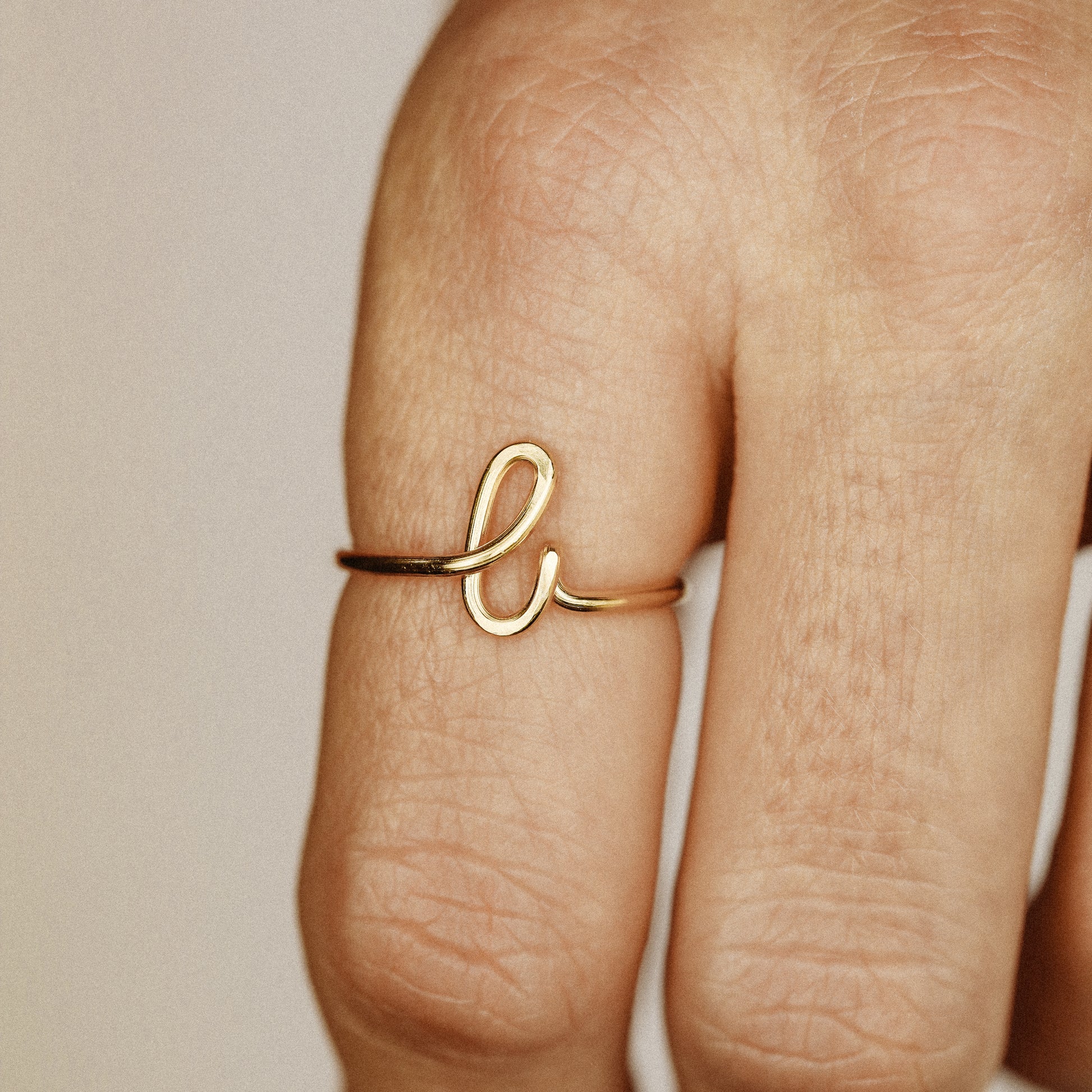 Close-up of a handmade 14k gold filled wire ring shaped into the letter L on a woman's finger.