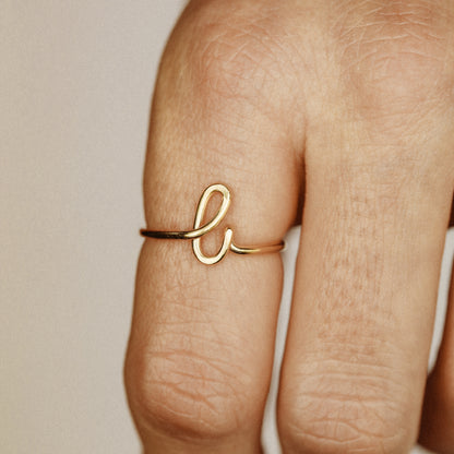Close-up of a handmade 14k gold filled wire ring shaped into the letter L on a woman's finger.