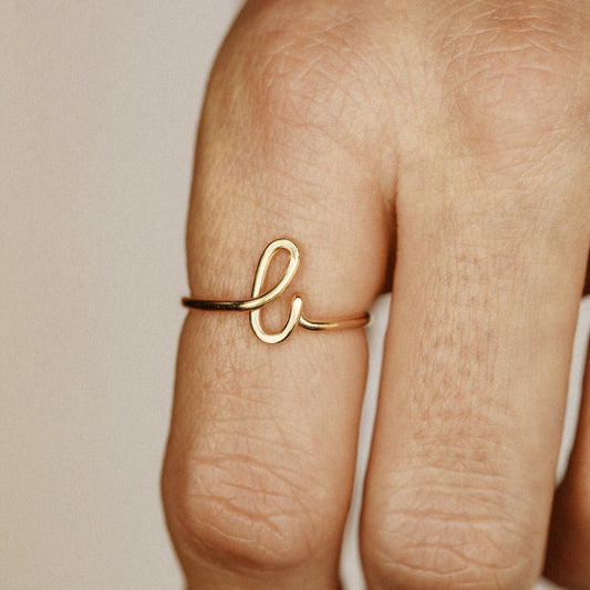 Close-up of a handmade 14k gold filled wire ring shaped into the letter L on a woman's finger.