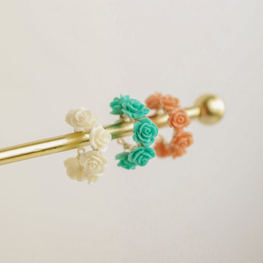 Floral resin rose conch ear cuffs displayed on a gold jewelry stand in white ivory, turquoise aqua blue and peach coral colors