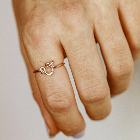 Close-up of a handmade 14k rose gold filled wire ring shaped into the letter V on a woman's finger.