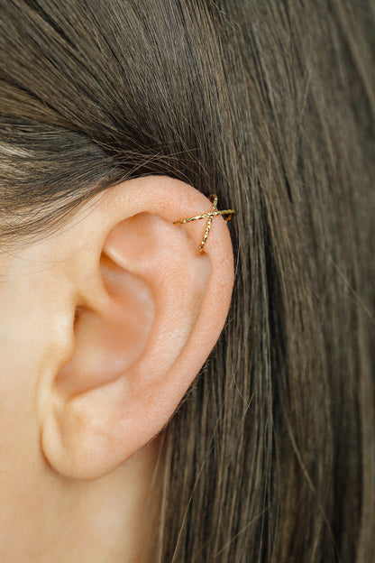Close-up of a person's ear wearing three textured gold diamond-cut ear cuffs on the helix, showing the adjustable fit and shimmering gold finish.