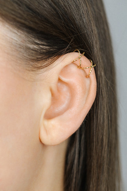 Close-up of a person's ear wearing three textured gold diamond-cut ear cuffs on the helix, showing the adjustable fit and shimmering gold finish.