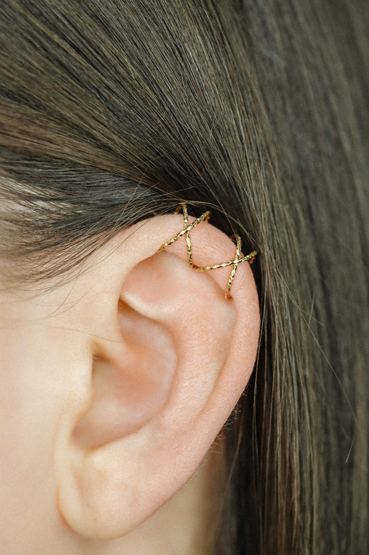 Close-up of a person's ear wearing three textured gold diamond-cut ear cuffs on the helix, showing the adjustable fit and shimmering gold finish.