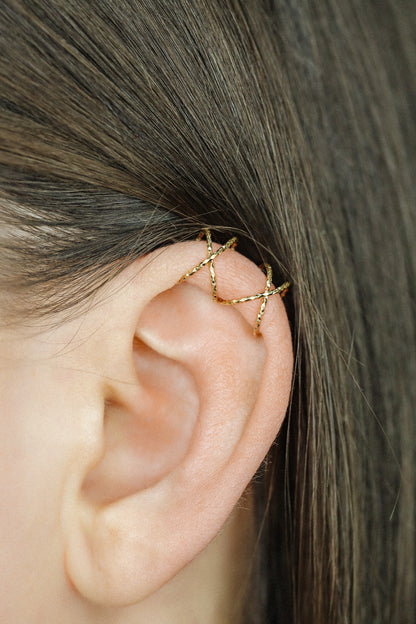 Close-up profile of a person's ear wearing a textured silver criss-cross ear cuff on the helix, handmade from diamond-cut 925 sterling silver.