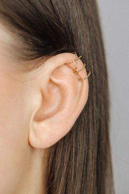 Close-up of a person's ear wearing three textured gold diamond-cut ear cuffs on the helix, showing the adjustable fit and shimmering gold finish.