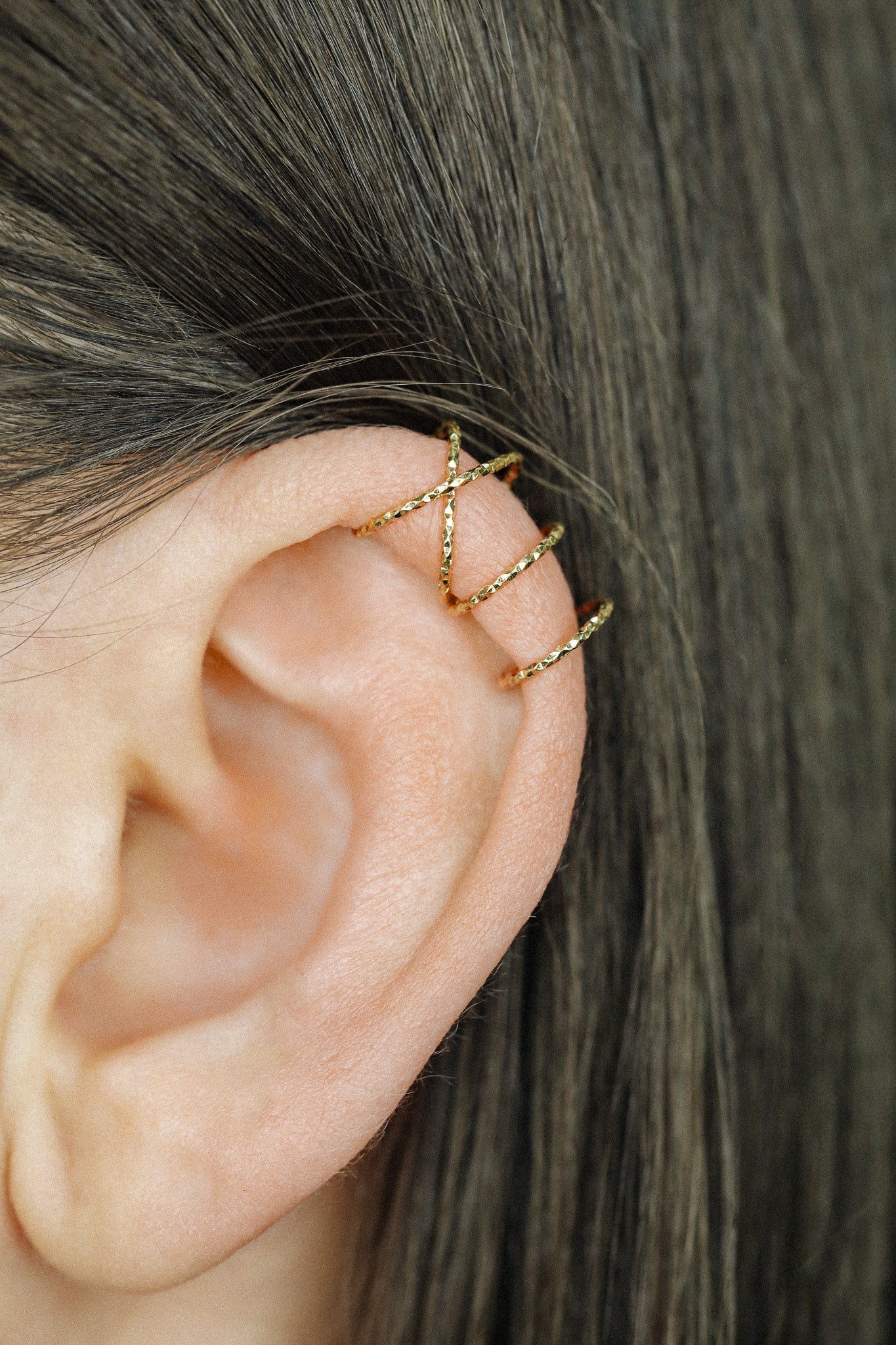 Close-up of a person's ear wearing three textured gold diamond-cut ear cuffs on the helix, showing the adjustable fit and shimmering gold finish.