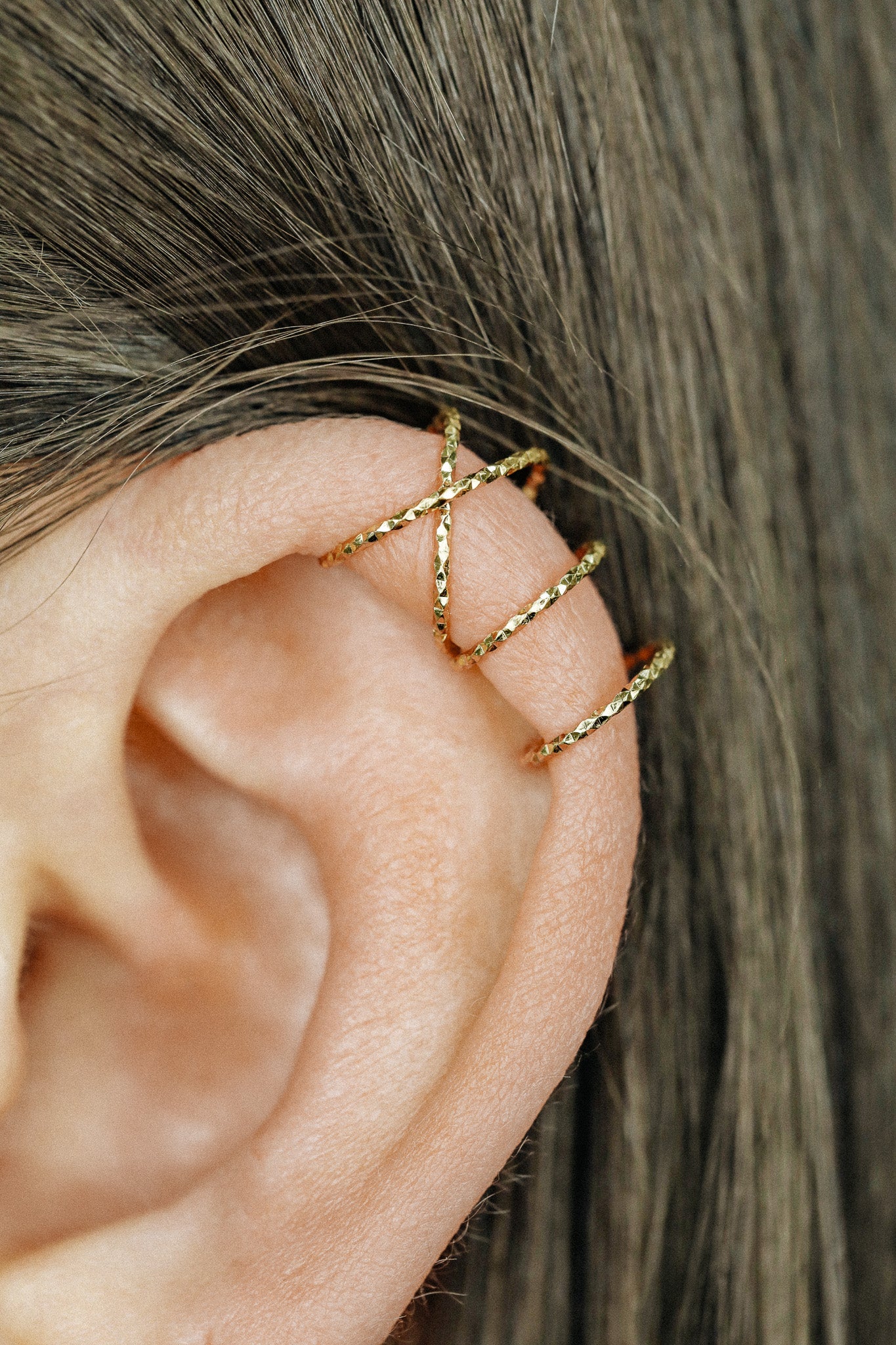 Close-up of a person's ear wearing three textured gold diamond-cut ear cuffs on the helix, showing the adjustable fit and shimmering gold finish.