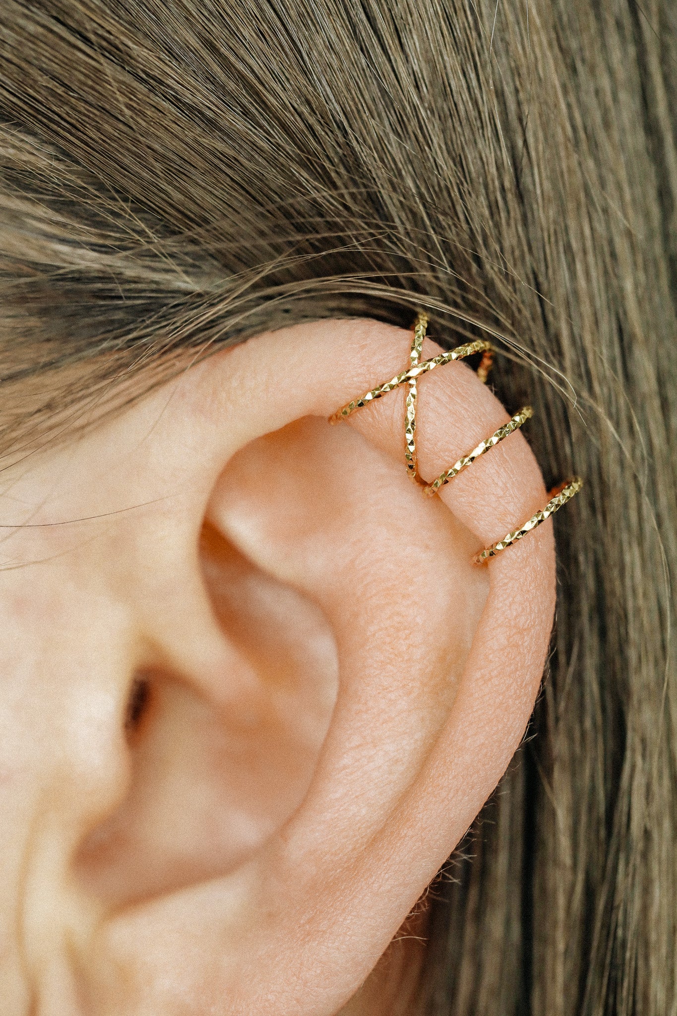 Close-up of a person's ear wearing three textured gold diamond-cut ear cuffs on the helix, showing the adjustable fit and shimmering gold finish.