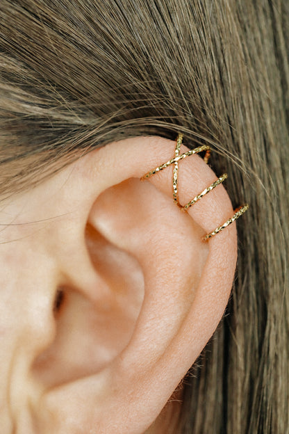 Close-up of a person's ear wearing three textured gold diamond-cut ear cuffs on the helix, showing the adjustable fit and shimmering gold finish.