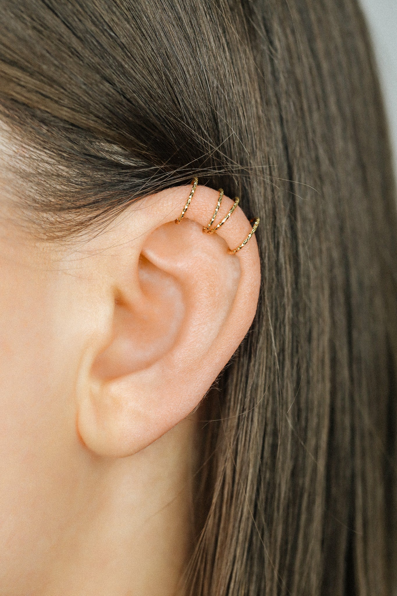 Close-up of a person's ear wearing three textured gold diamond-cut ear cuffs on the helix, showing the adjustable fit and shimmering gold finish.
