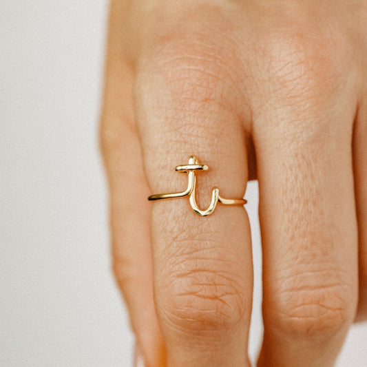 Close-up of a handmade 14k gold filled wire ring shaped into the letter T on a woman's finger.