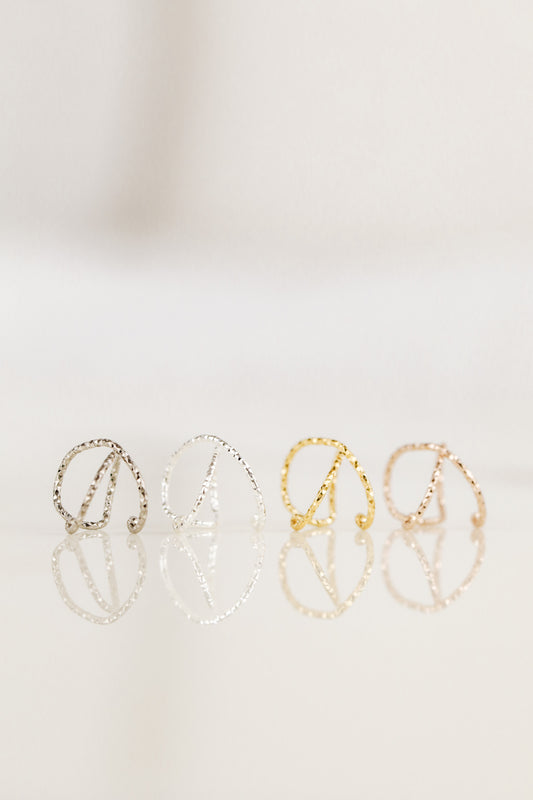 Close-up of a person wearing a textured black ruthenium criss-cross ear cuff and a double hoop cuff on the upper helix, handmade jewelry without piercing.