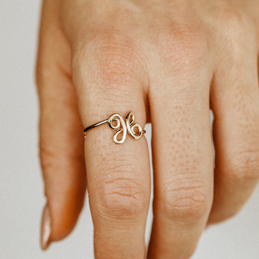 Handmade adjustable wire ring featuring a lowercase cursive letter X in gold on a person's hand with red tipped nails.