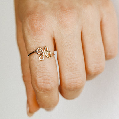 Close-up of a handmade 14k gold filled wire ring shaped into the letter X on a woman's finger.
