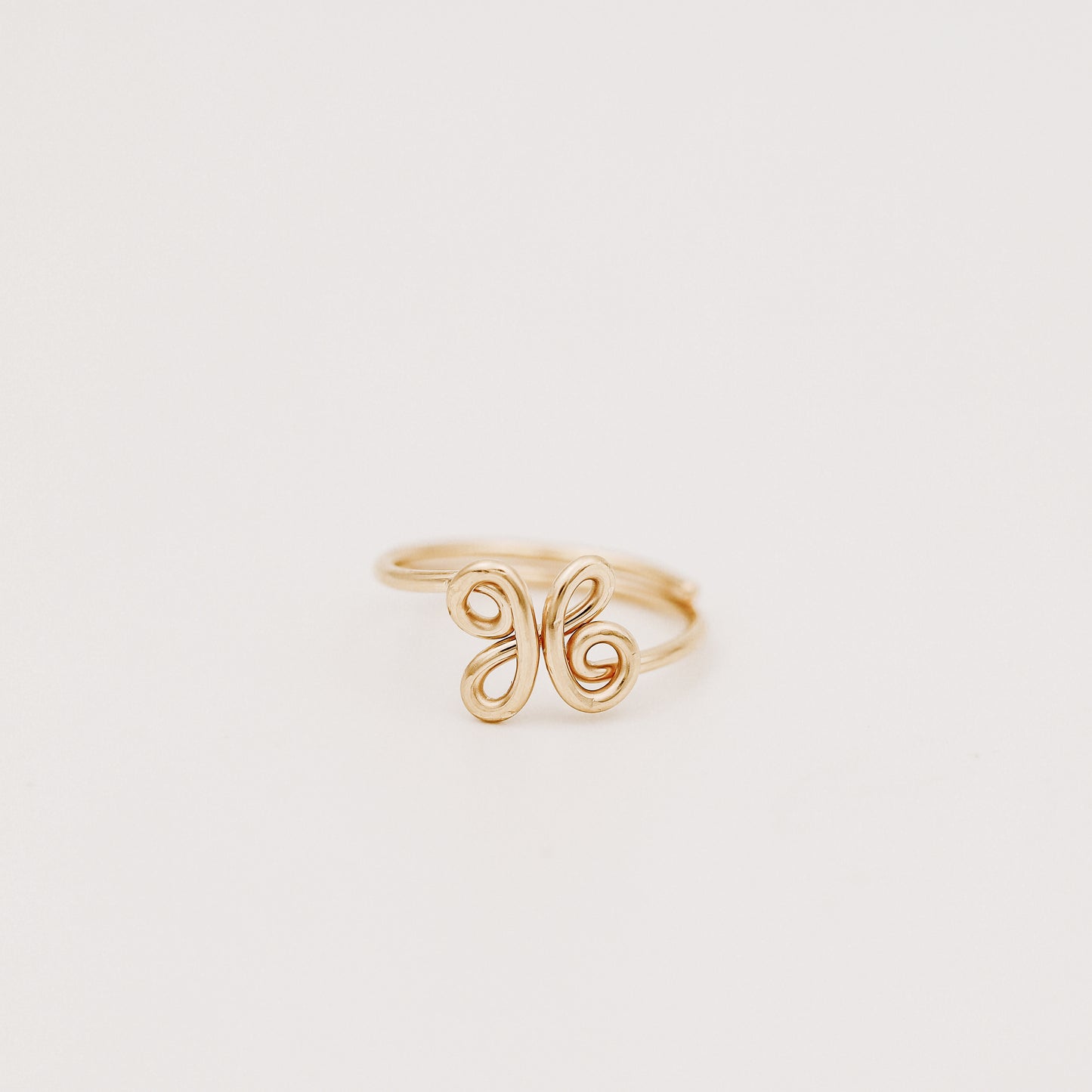 Handmade adjustable wire ring featuring a lowercase cursive letter X in gold on a person's hand with red tipped nails.
