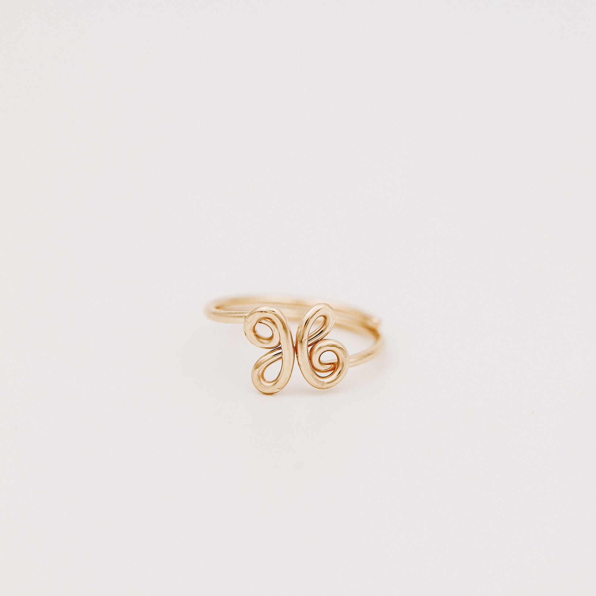 Handmade adjustable wire ring featuring a lowercase cursive letter X in gold on a person's hand with red tipped nails.