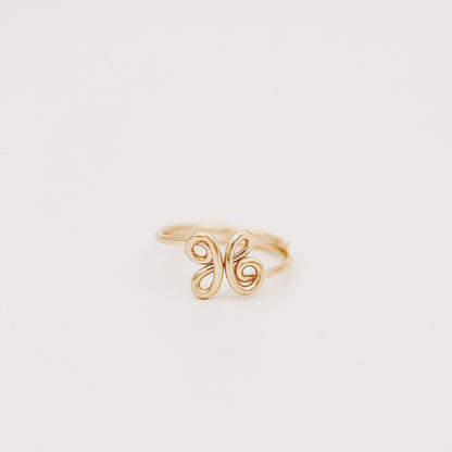 Handmade adjustable wire ring featuring a lowercase cursive letter X in gold on a person's hand with red tipped nails.