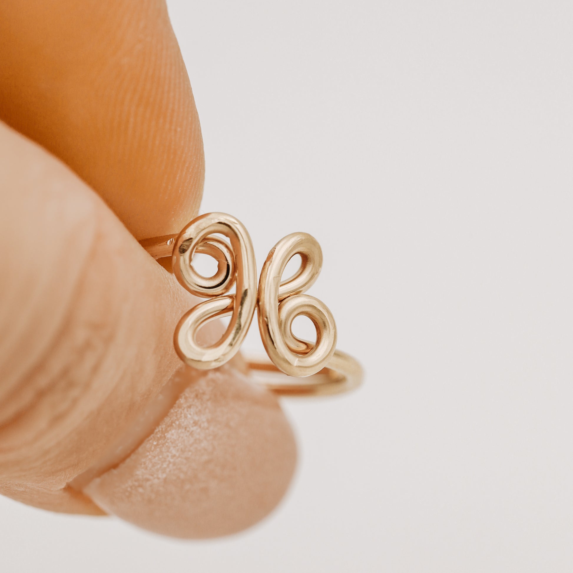 Handmade adjustable wire ring featuring a lowercase cursive letter X in gold on a person's hand with red tipped nails.