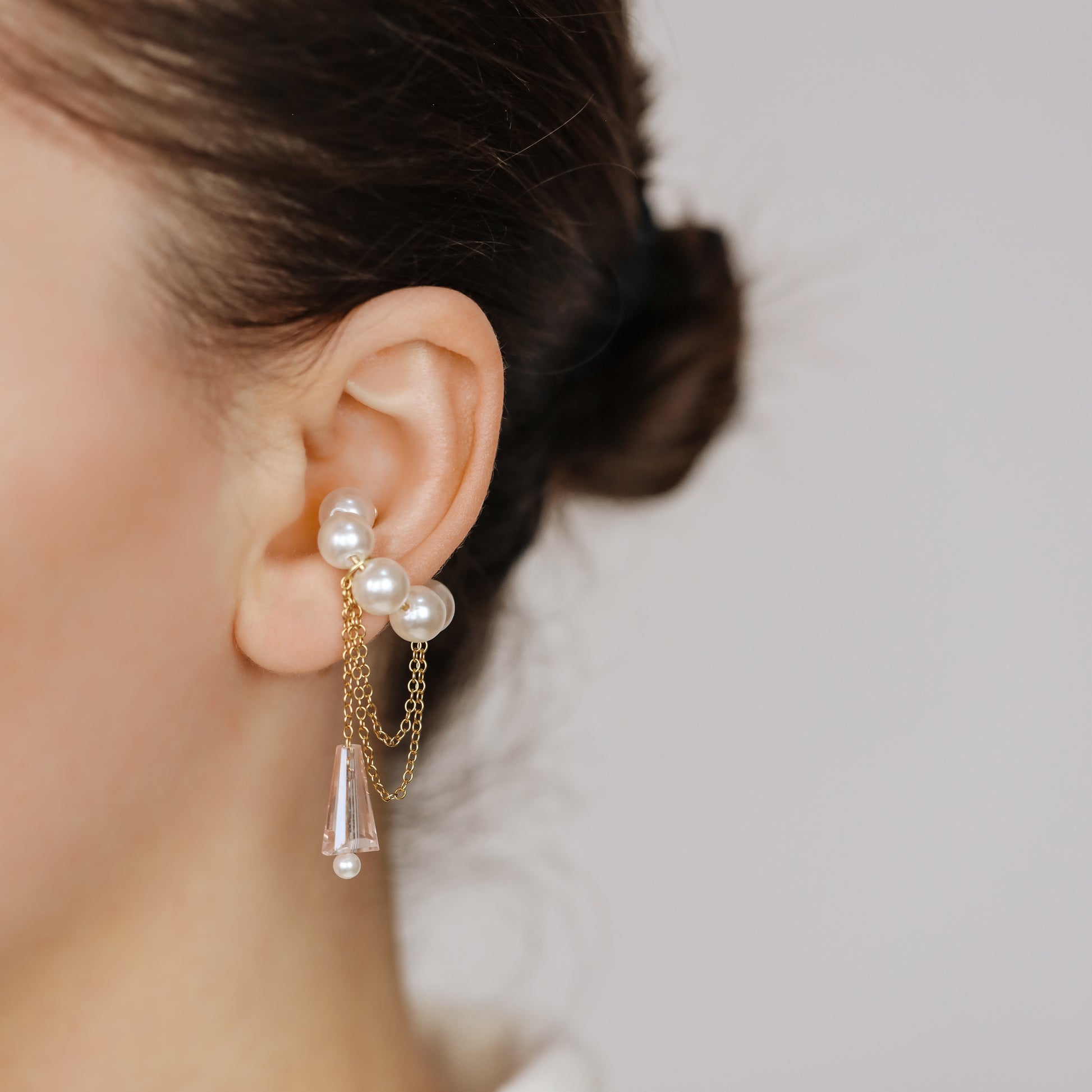 Dainty pearl crystal conch ear cuff shown as a no-piercing cartilage accessory, featuring artificial pearls around the conch area, delicate draped chains and a dangling faceted crystal drop, handmade and available in sterling silver 925, 14k gold filled or 14k rose gold filled.