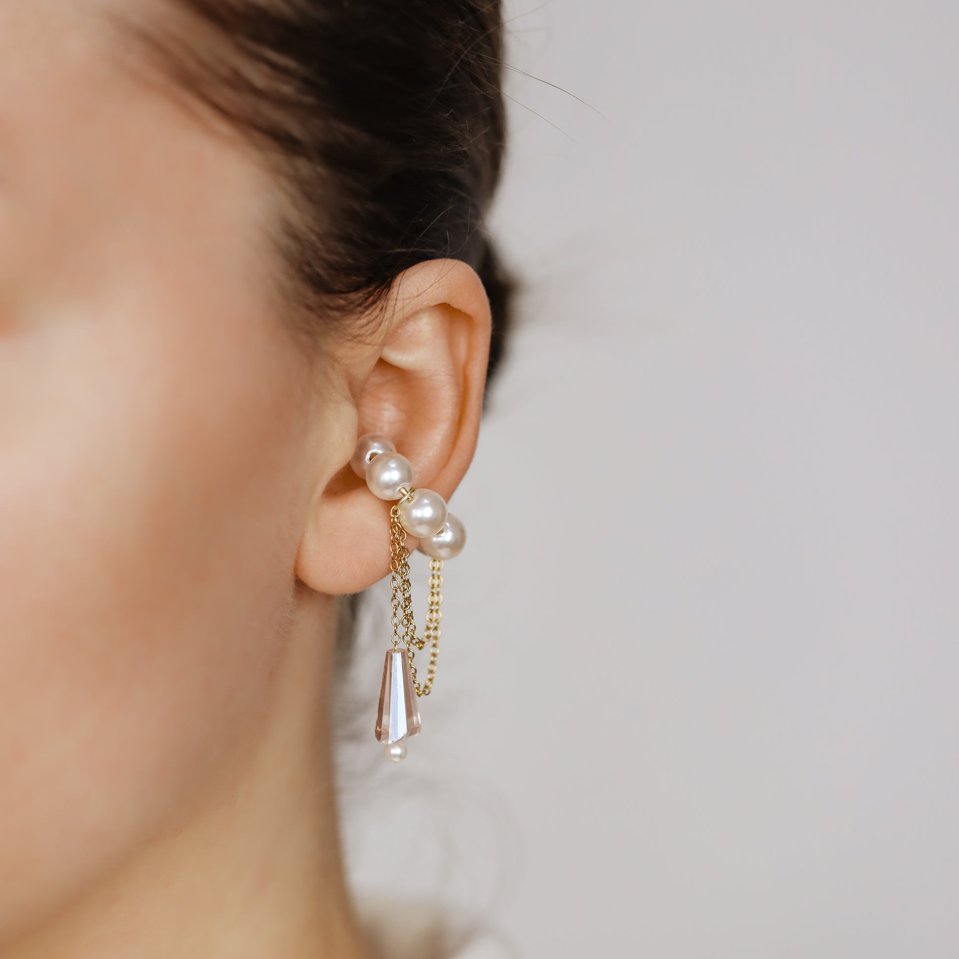 Dainty pearl crystal conch ear cuff shown as a no-piercing cartilage accessory, featuring artificial pearls around the conch area, delicate draped chains and a dangling faceted crystal drop, handmade and available in sterling silver 925, 14k gold filled or 14k rose gold filled.