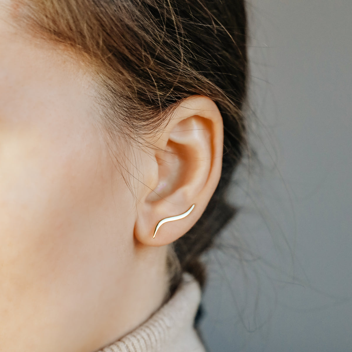 Gold wave ear climber worn across the lower ear, showing how the curved earring rises naturally along the lobe after being inserted through one standard piercing.