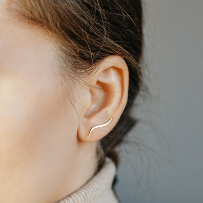 Gold wave ear climber worn across the lower ear, showing how the curved earring rises naturally along the lobe after being inserted through one standard piercing.