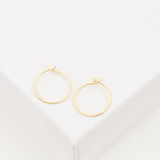 Minimal thin gold wire hoop earrings displayed on soft white fabric