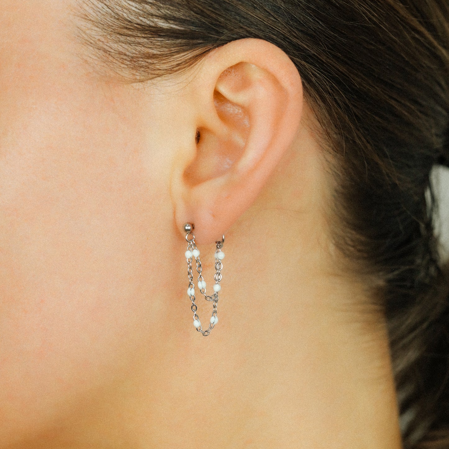 Silver double chain dangle earrings worn on ear with white bead accents