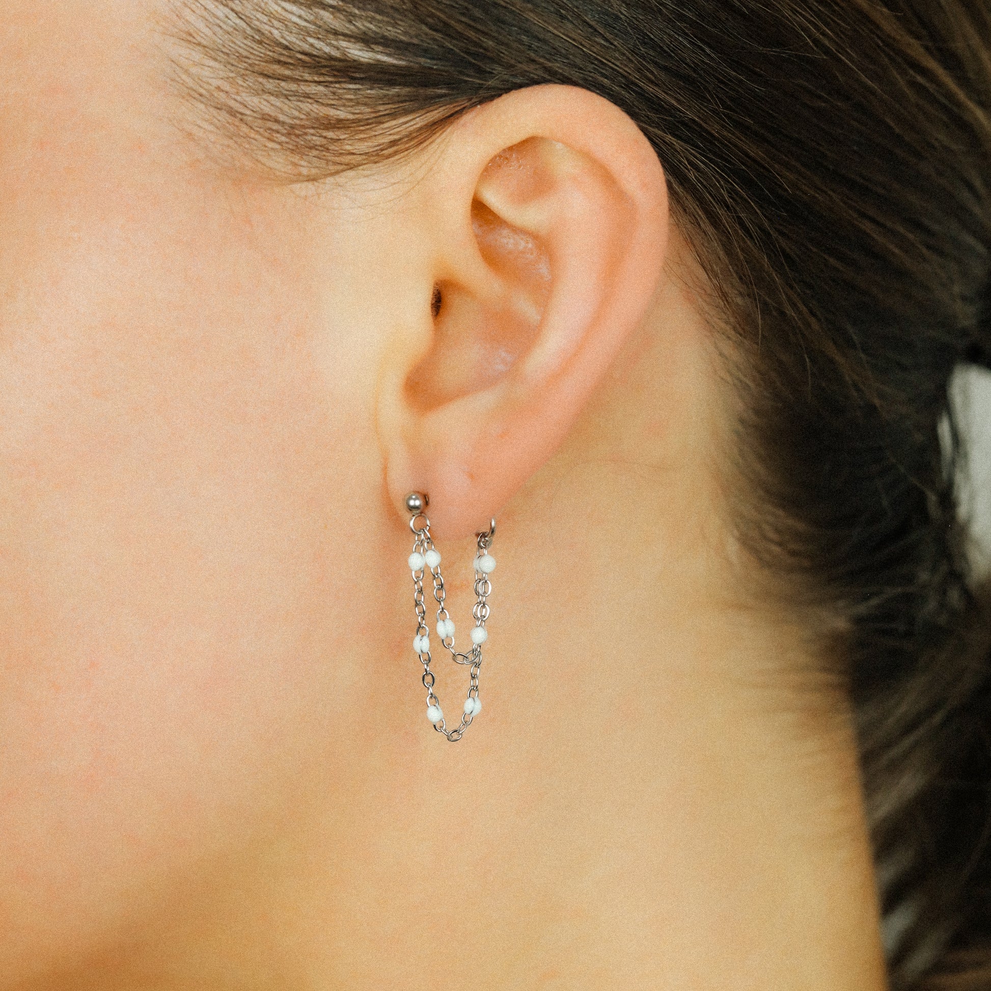 Silver double chain dangle earrings worn on ear with white bead accents