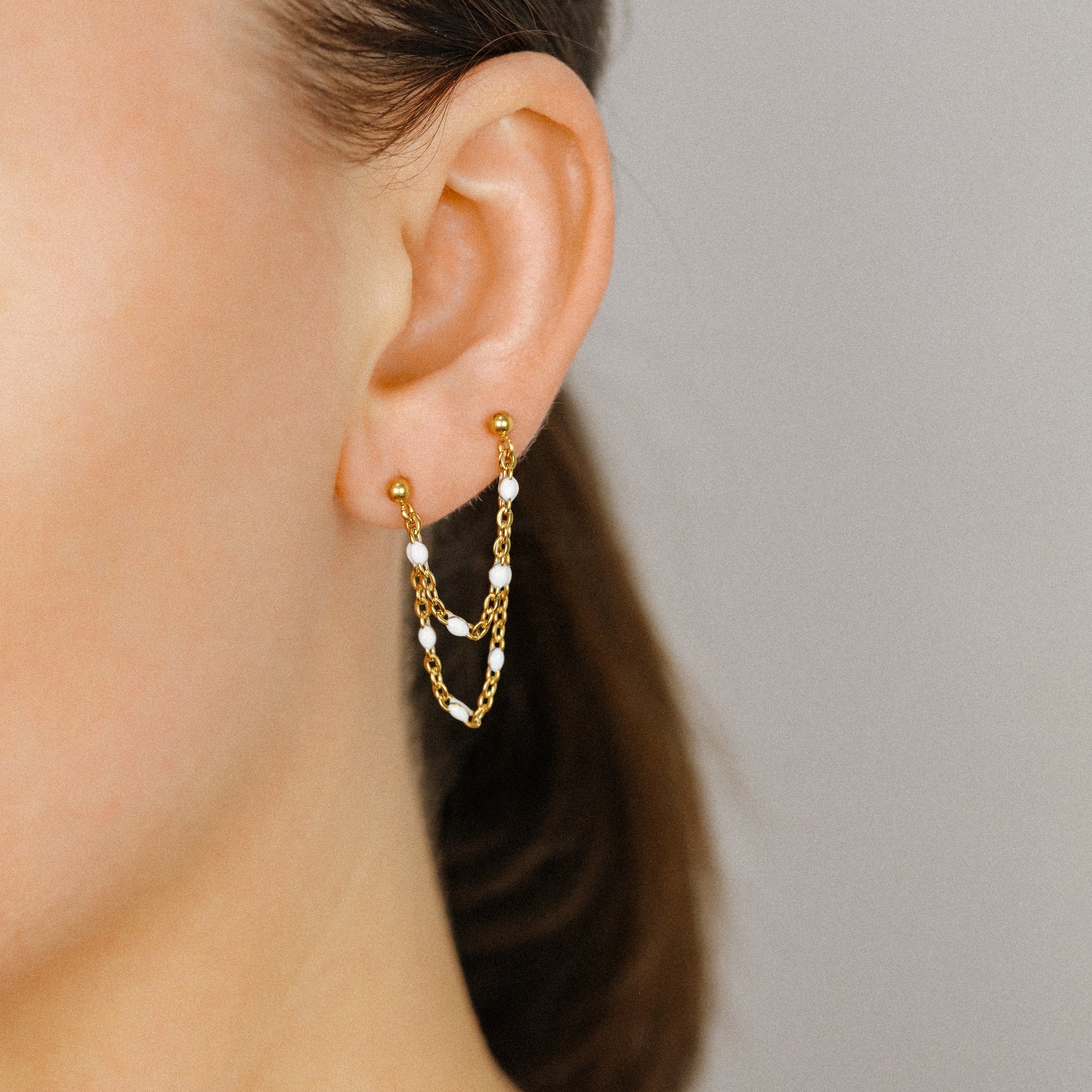 Gold double chain stud earring worn on two lobe piercings with white bead details