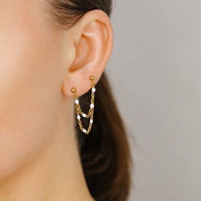 Gold double chain stud earring worn on two lobe piercings with white bead details