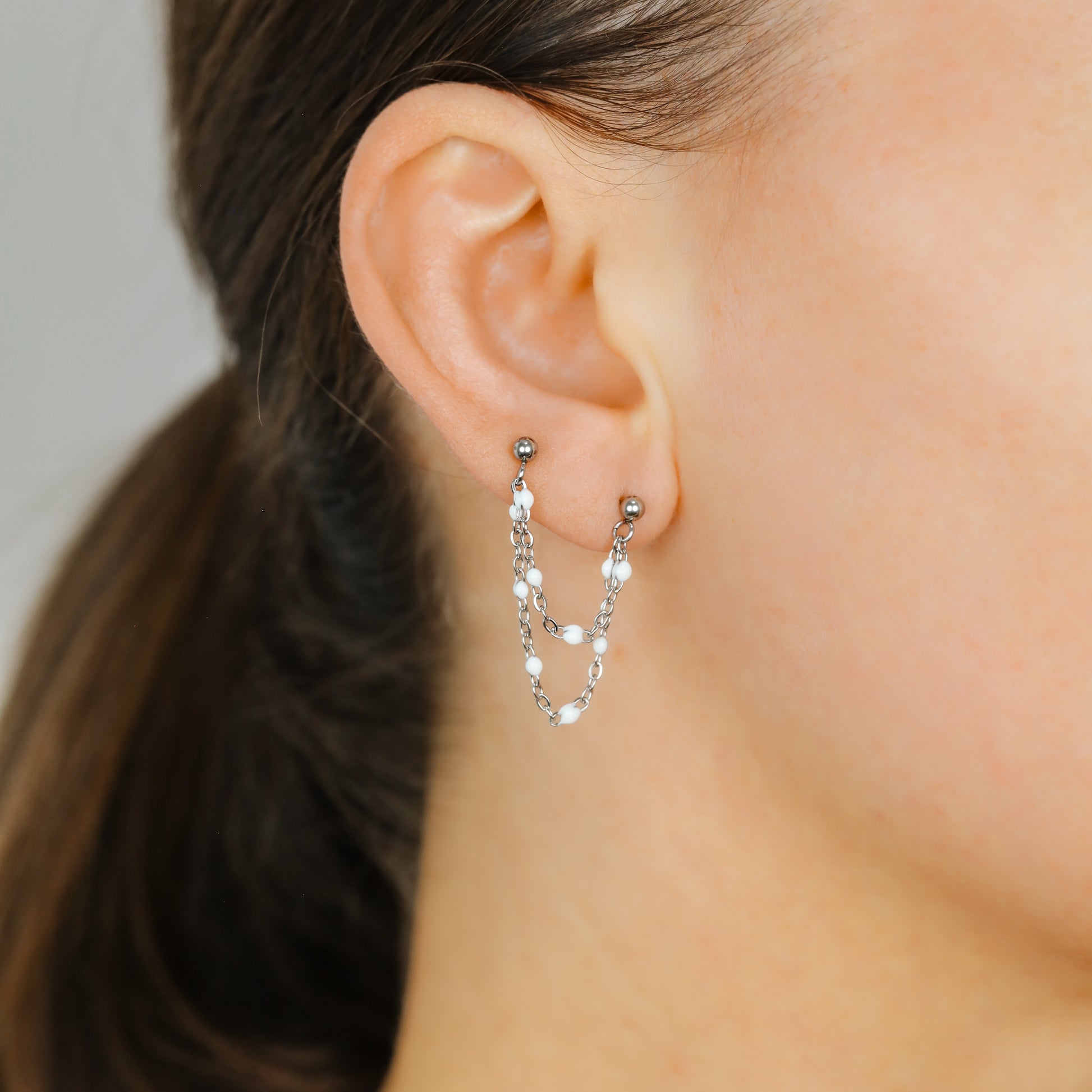 Silver double chain stud earring worn on two lobe piercings with white enamel beads